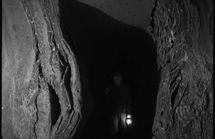 Zarys postaci z zapaloną lampą w ciemnej wnęce w kopalni.